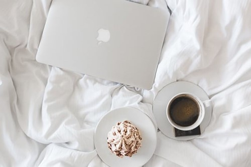 A laptop, coffee, and cake on a bed.